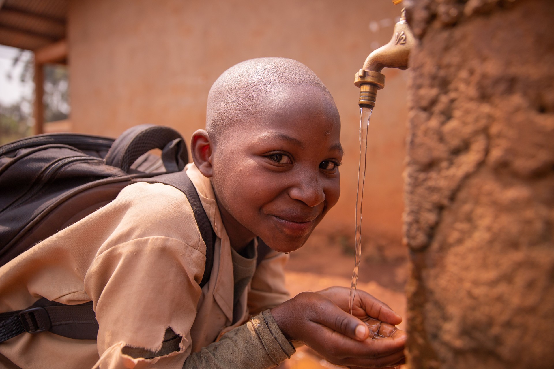 Black schoolchild collects water with his hands from the tap located in the schoolyard. Water concept